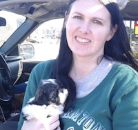 a woman sitting in a car holding a small puppy