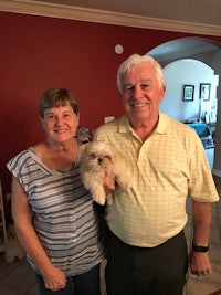 an older couple holding a white dog in a living room