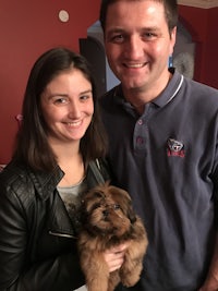 a man and woman smiling while holding a small dog