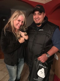 a man and woman holding a bag with a small dog in it