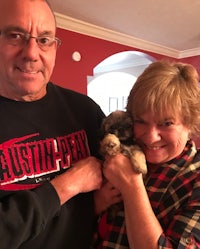 a man and woman holding a puppy in their living room